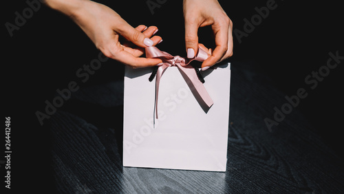 Tie a bow on a white gift bag. Women with beautiful manicure. White paper beg with pink bow. 