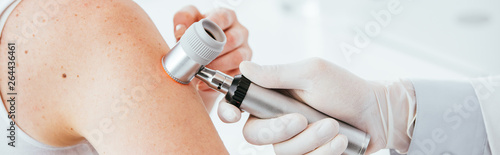 panoramic shot of dermatologist in latex glove holding dermatoscope while examining patient