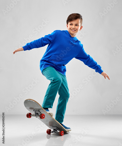 childhood, leisure and people concept - smiling boy in blue hoodie with skateboard over grey background