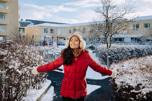 beautiful asian filipino girl in her 20s with her eyes closed with her beautiful smile breathing in fresh air in Iceland and enjoying the winter snow while wearing a beanie and red jacket with gloves