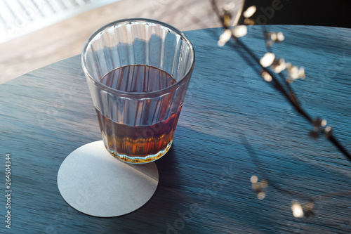 Transparent glass with tea and beer coaster on wooden table. 3d rendering.