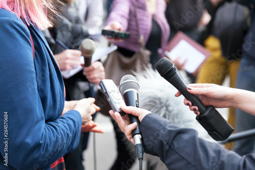 Public figure talking to the media, journalists holding microphones at press conference