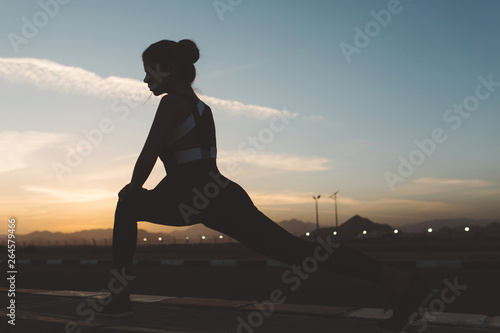 Amazing young woman in sporstwear stretching on road on sunset background. Silhouette of attractive figure, active lifestyle, workout in summer, enjoying sport, yoga, hardworking sporstwoman