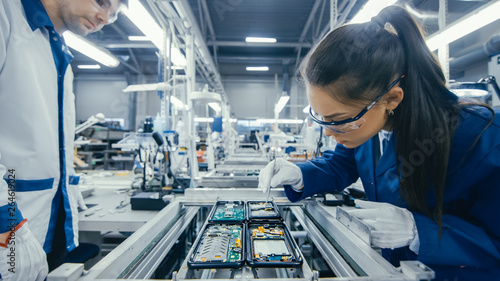 Shot of an Electronics Factory Workers Assembling Circuit Boards by Hand While it Stands on the Assembly Line. High Tech Factory Facility.