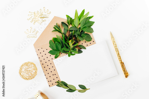 Styled desk with envelope, blank card, composition of green leaves and gold office stuff. Flat lay.