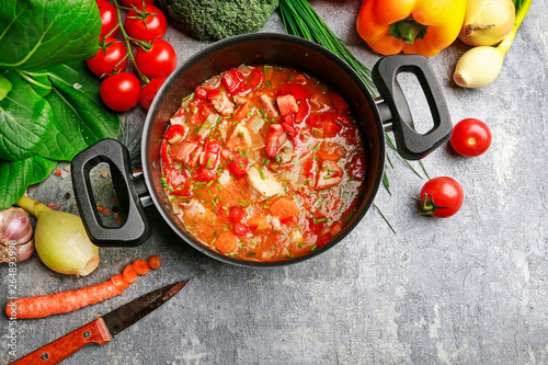 Goulash soup and colorful vegetables on grey stone background.