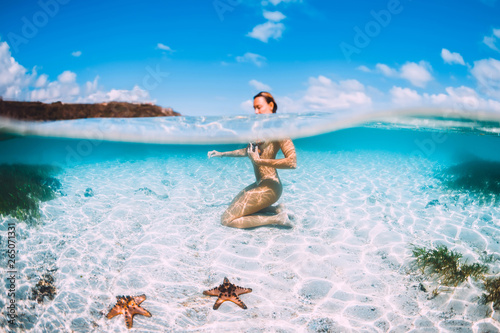 Naked woman swim in blue ocean with starfish, underwater in tropical sea