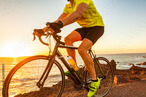 Bike race at sunset road biking cyclist riding bicycle outdoor with sun flare closeup of legs and yellow cycle shoes.