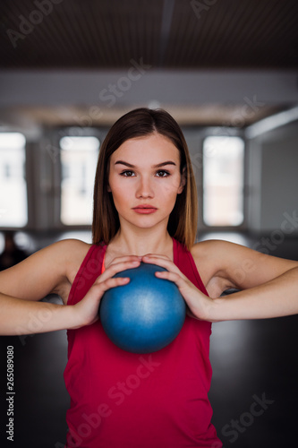 A portrait of young girl or woman doing exercise with a ball in a gym.