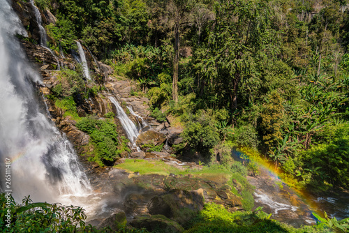 Massive water stream falling in tropical forest with parts of rainbow 