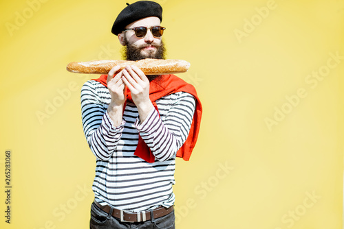 Portrait of a stylish man dressed in french style with striped shirt, hat and red scarf on the yellow background