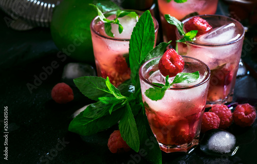 Alcoholic cocktail raspberry mojito with berry, lime, syrup, soda, rum, mint and crushed ice. Steel bar tools, black bar counter, selective focus