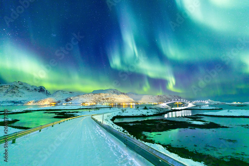 Aurora Borealis natural phenomenon on Lofoten Islands in Norway, Scandinavia, Europe. Night sky with northern lights over mountains and road reflected in fjord. Night winter landscape with aurora.