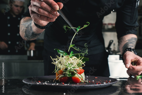 Chef finishing healthy salad on a black plate with tweezers. almost ready to serve it on a table