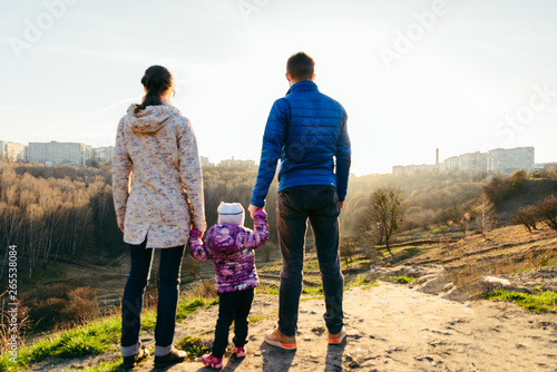 young family of three standing on the top of the hill with beautiful view of sunset