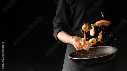 Seafood, Professional cook prepares shrimps with sprigg beans. Cooking seafood, healthy vegetarian food and food on a dark background. Horizontal view. Eastern kitchen