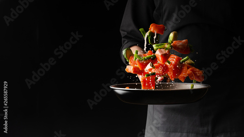 Chef prepares pieces of salmon or trout fillet with green beans in a pan, on a black background for design, recipe book, menu, restaurant or hotel sign, cooking, gastronomy