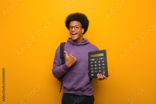 Young african american student man holding a calculator surprised, feels successful and prosperous