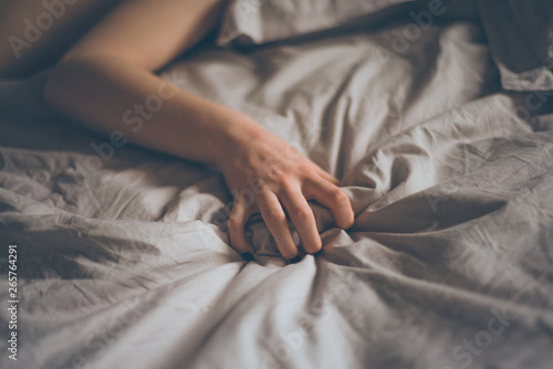 Hand sign orgasm of woman on white bed. Hand of female pulling white sheets in ecstasy. Feeling and emotion concept. Love sex concept.