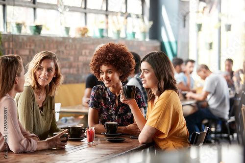 Four Young Female Friends Meeting Sit At Table In Coffee Shop And Talk