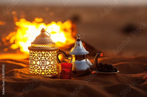Dates, teapot, cup with tea near the fire in the desert with a beautiful background. Ramadan Kareem