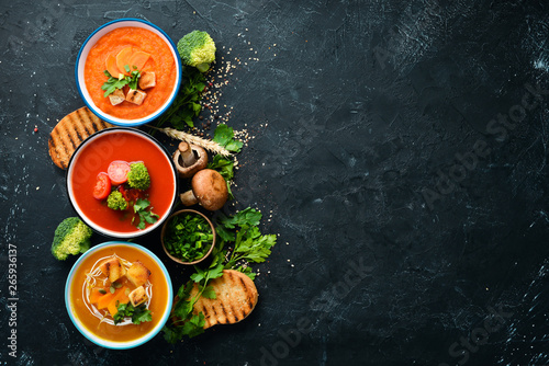 Assortment of colored vegetable cream soups. Dietary food. On a black stone background. Top view. Free copy space.