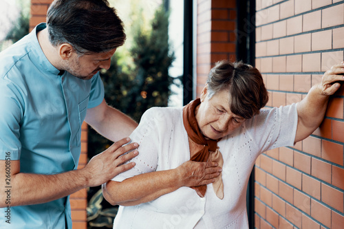 Male nurse helping sick elderly woman with chest pain