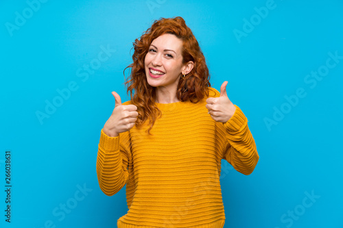 Redhead woman with yellow sweater with thumbs up gesture and smiling