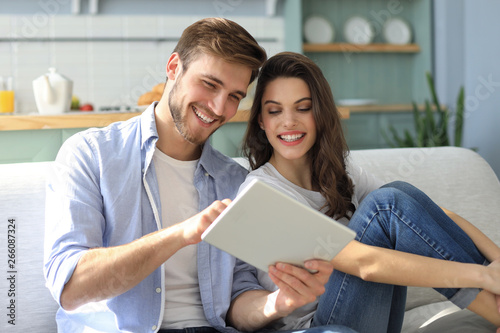 Young couple watching media content online in a tablet sitting on a sofa in the living room.