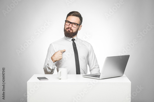 Portrait of satisfied confident smiling bearded young manager in white shirt and black tie are sitting in office are prouded of himself for achieved goals in work. Studio shot, indoor, isolated