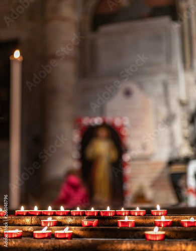 Candele e lumini di devozione e preghiera dei fedeli sullo sfondo di un altare sacro di una chiesa, con immagini sacre e di santi in preghiera