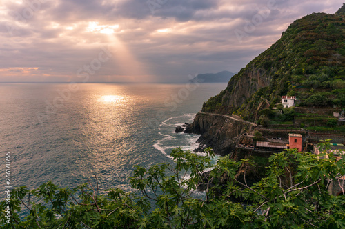 Crepuscular sun rays beaming through the thick clouds at sunset and getting reflected by the Mediterranean Sea waters on the Ligurian coast in Riomaggiore, Italy.