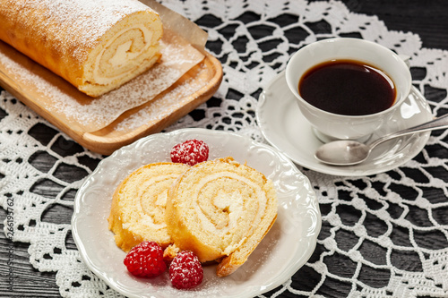 Ciasto - rolada biszkoptowa z kremem mascarpone na talerzyku, obok kawa w filiżance, wszystko postawione na koronkowej serwetce