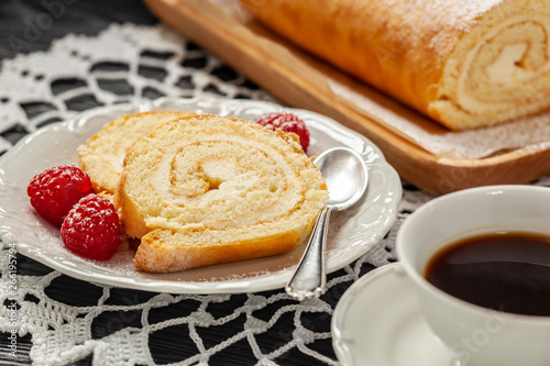 Ciasto - rolada z kremem mascarpone na talerzyku, obok kawa w filiżance, wszystko postawione na koronkowej serwetce