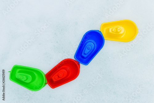 Plastic multicolored toy boats on foam bath.