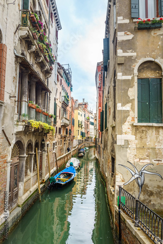 view on famous Grand Canal among historic houses in Venice, Italy at cloudy day with dramatic sky, wood bridge and sitting woman on the foreground.