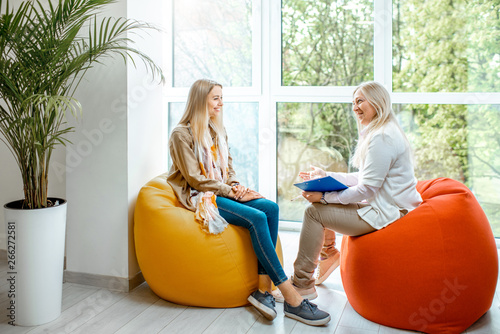 Young woman with senior female psychologist or mental coach sitting on the comfortable chairs during the psychological counseling in the office