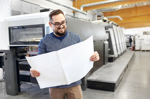 Printing house. Satisfied man is watching the printout.