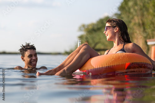 Group of friends swimming and having fun in the lake.Female sitting on air mattress drinks lemonade and having fun with friends.