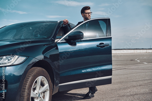 On the way to business meeting. Handsome young businessman entering his car while standing outdoors