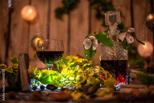 Red wine and green ivy on a wooden table in front of a wooden background with a creative lighting