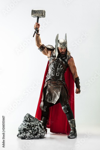Long hair and muscular male model in leather viking's costume with the big hammer cosplaying Thor isolated on white studio background. Full-lenght portrait. Fantasy warrior, antique battle concept.