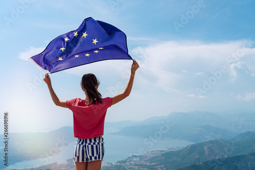 Child girl teenager young person is waving European Union flag on top of mountain at sky background