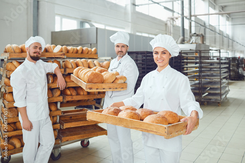 Bakers hold a tray with fresh bread in the bakery.