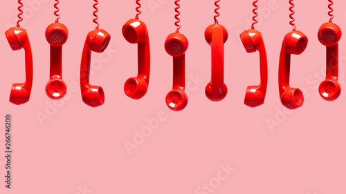 Various views of old red telephone receivers hanging on pink background