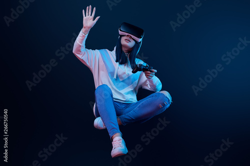woman holding joystick and levitating while gesturing and wearing virtual reality headset on blue