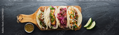 four mexican street tacos with fish barbacoa and carnitas shot in panoramic composition on top of serving wooden board