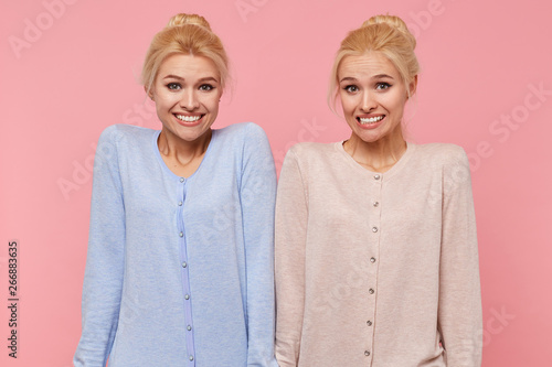 Beautiful young blonde twins confused and unable to explain and understand the current situation, shrug and smile isolated over pink background.