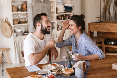 Image of modern brunette couple eating breakfast together while sitting at table at home