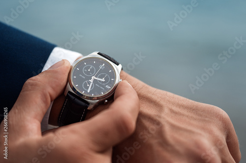 A man in a business suit checking a wrist watch on his hand on background sea